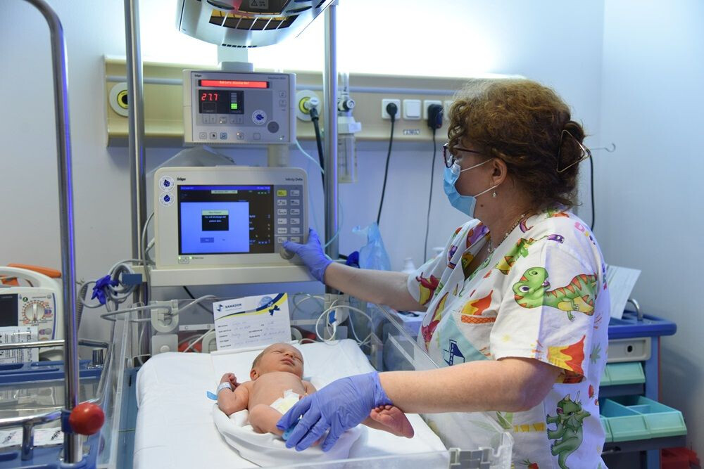 Nou-născut conectat la monitor care arată semnele vitale, îngrijit de o asistentă.